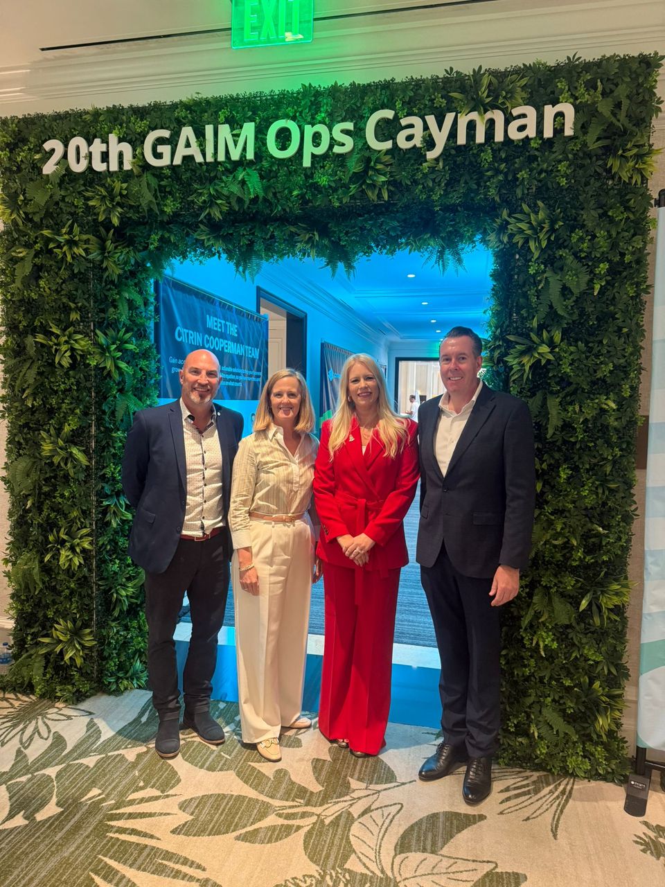 Four panel participants standing in front of the green-wall “20th GAIM Ops Cayman” sign