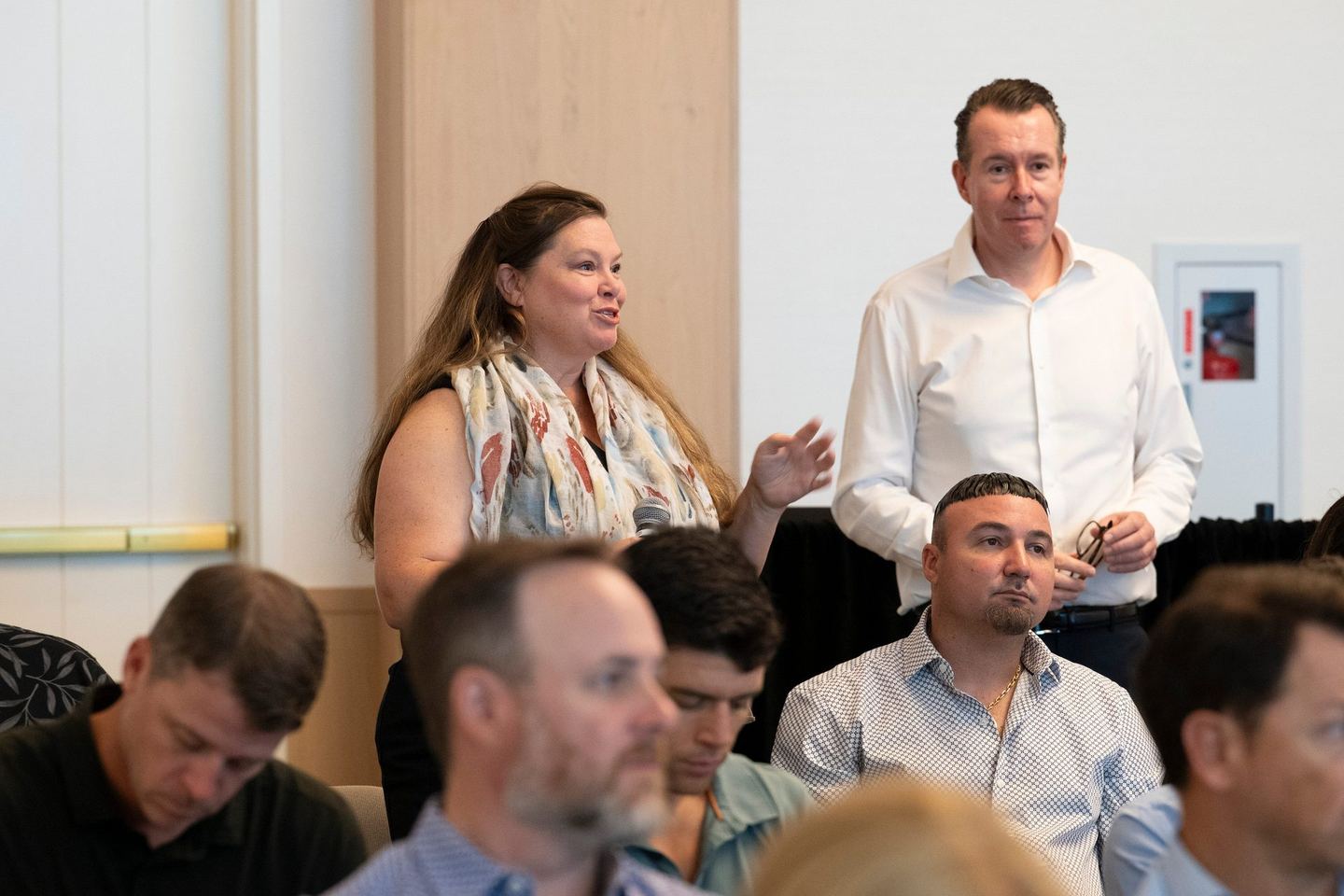 Delegates seated at a table during a discussion, one speaking while a colleague stands behind