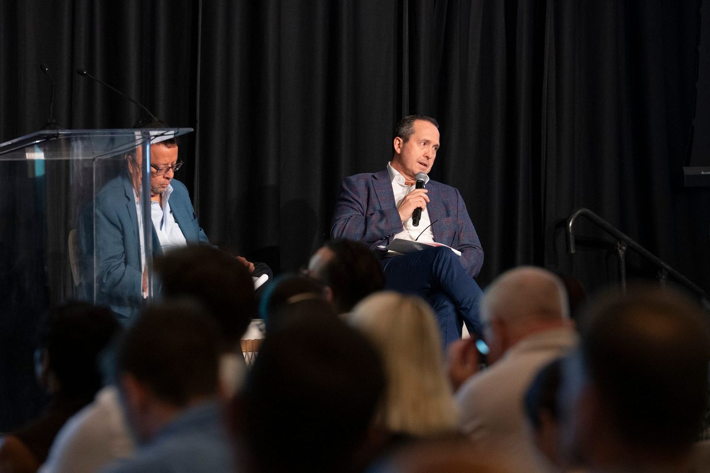 Panellists seated on stage, one speaking into a microphone, seen over the audience